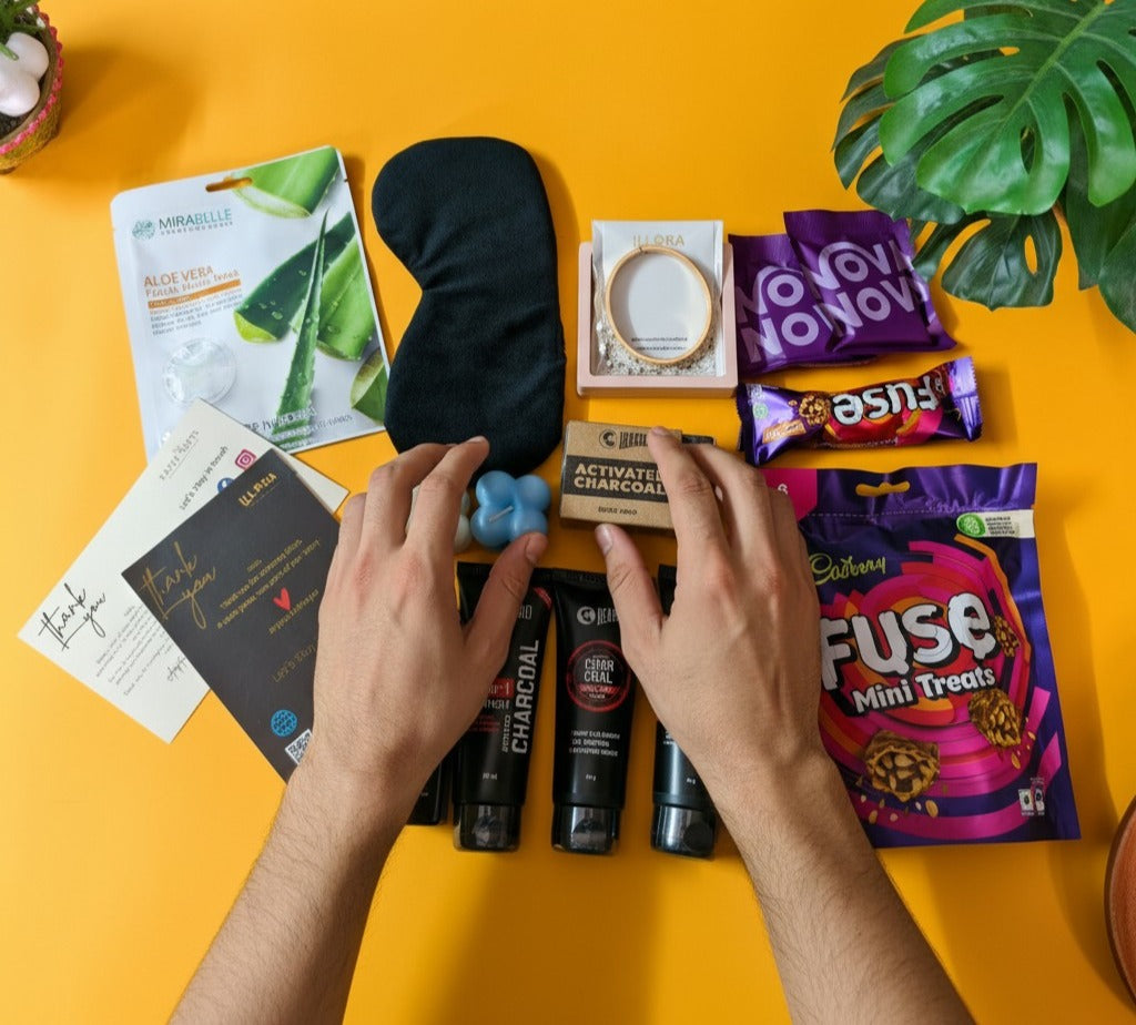 The Alfa Glow Grooming & Self-Care Gift Hamper For Men containing Beardo Grooming kit, Anti-tarnish jewellery, and sweet treats on a yellow table