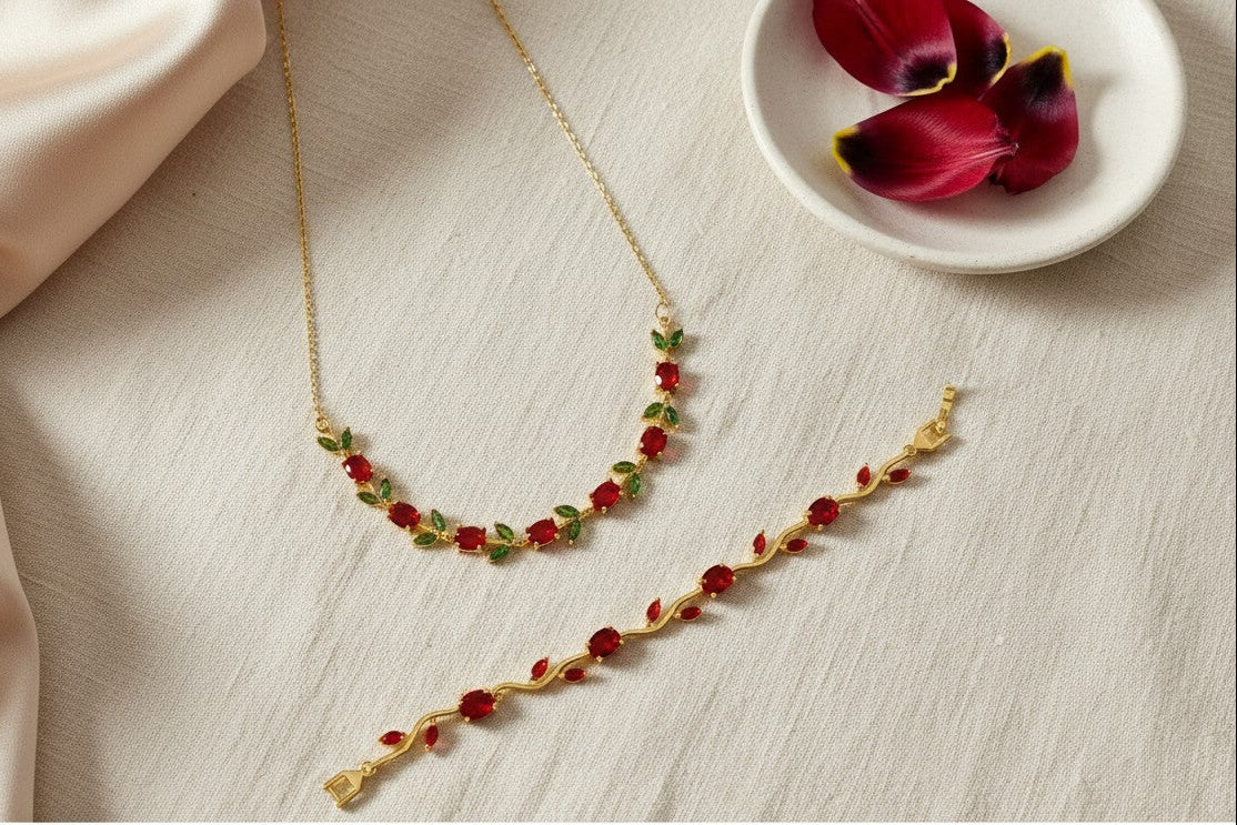 Anti-tarnish, gold-plated Tulip Necklace & Bracelet Set with Red & Olive Green stones on a light surface with a plate of flowers.
