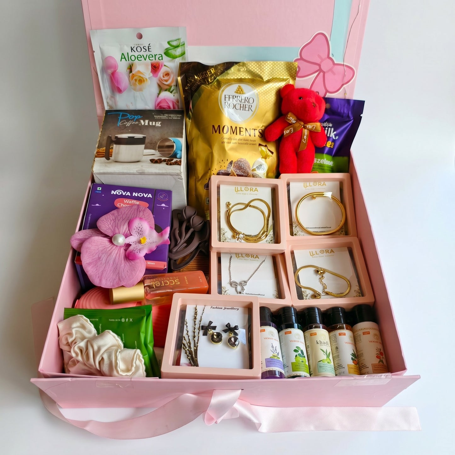 Gift Hamper For Women and girls with travel care products, accessories, teddy key chain, sweet treats, and jewellery on a white background