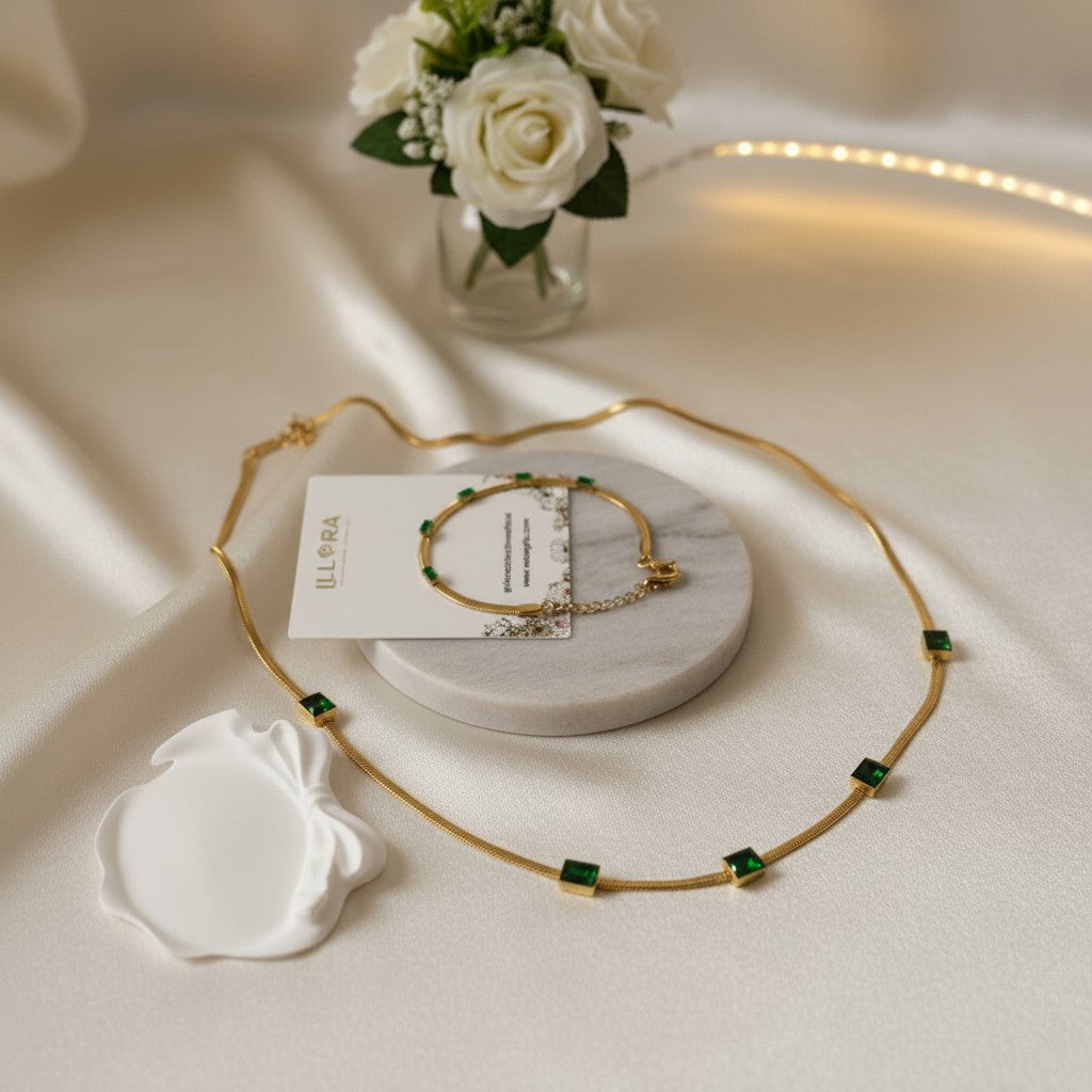 Emerald Whisper Serpentine Set – Gold-plated Green Emerald Stone Embedded Snake Necklace & Snake Bracelet Set on a white surface with a vase of flowers in the background