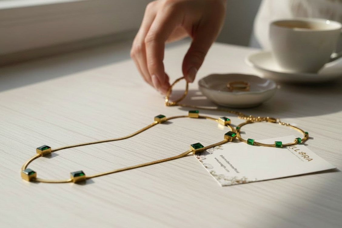 Gold-plated Green Emerald Stone Embedded Snake Necklace & Snake Bracelet Seton a light surface, with a hand and coffee cup in the background.