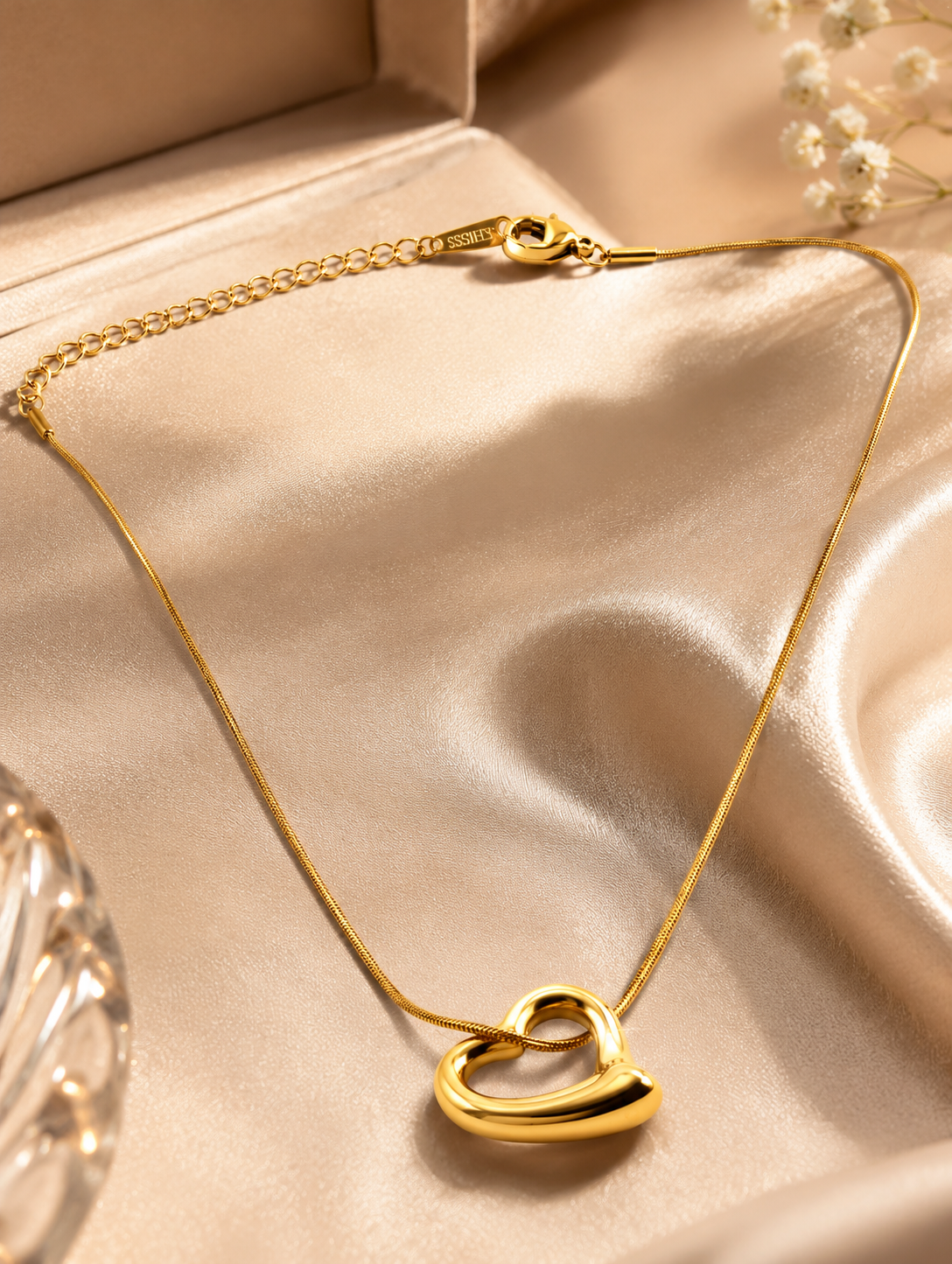 A Gold Plated Anti Tarnish Tilted Heart Necklace displayed on a beige satin fabric inside an open jewellery box.