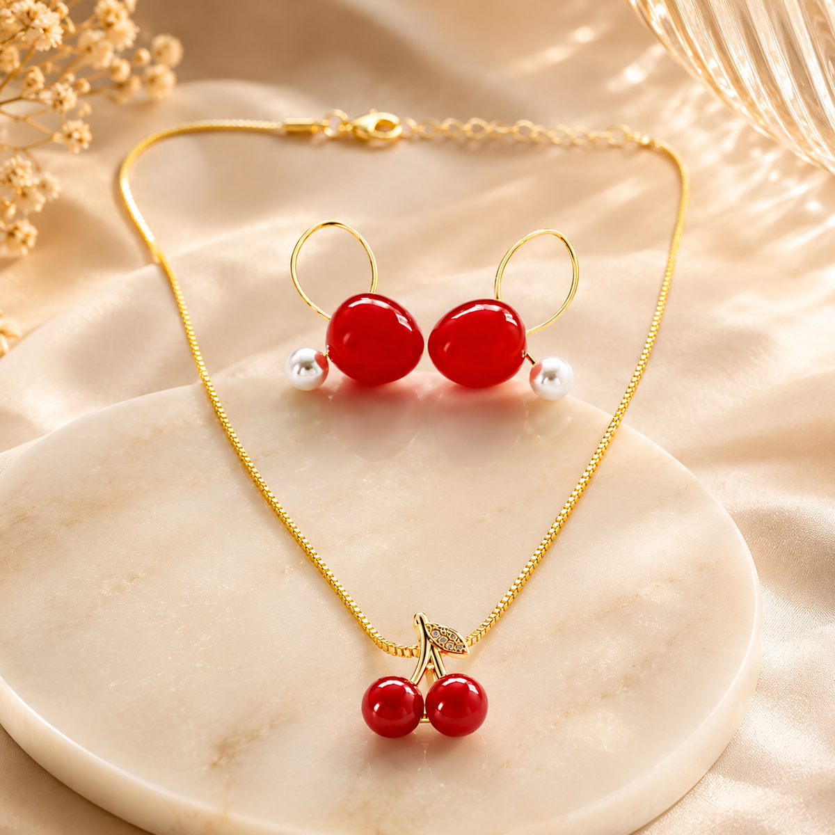 Cherry Bloom Gold Toned Necklace & Earrings Set for women arranged on a cream marble slab with soft beige fabric and dried flowers in the background.