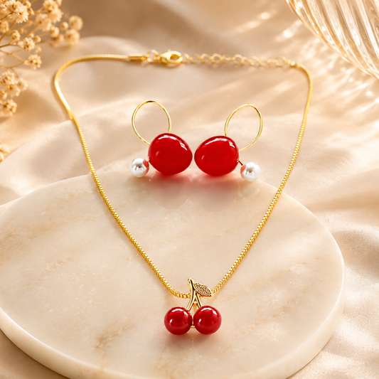 Cherry Bloom Gold Toned Necklace & Earrings Set for women arranged on a cream marble slab with soft beige fabric and dried flowers in the background.