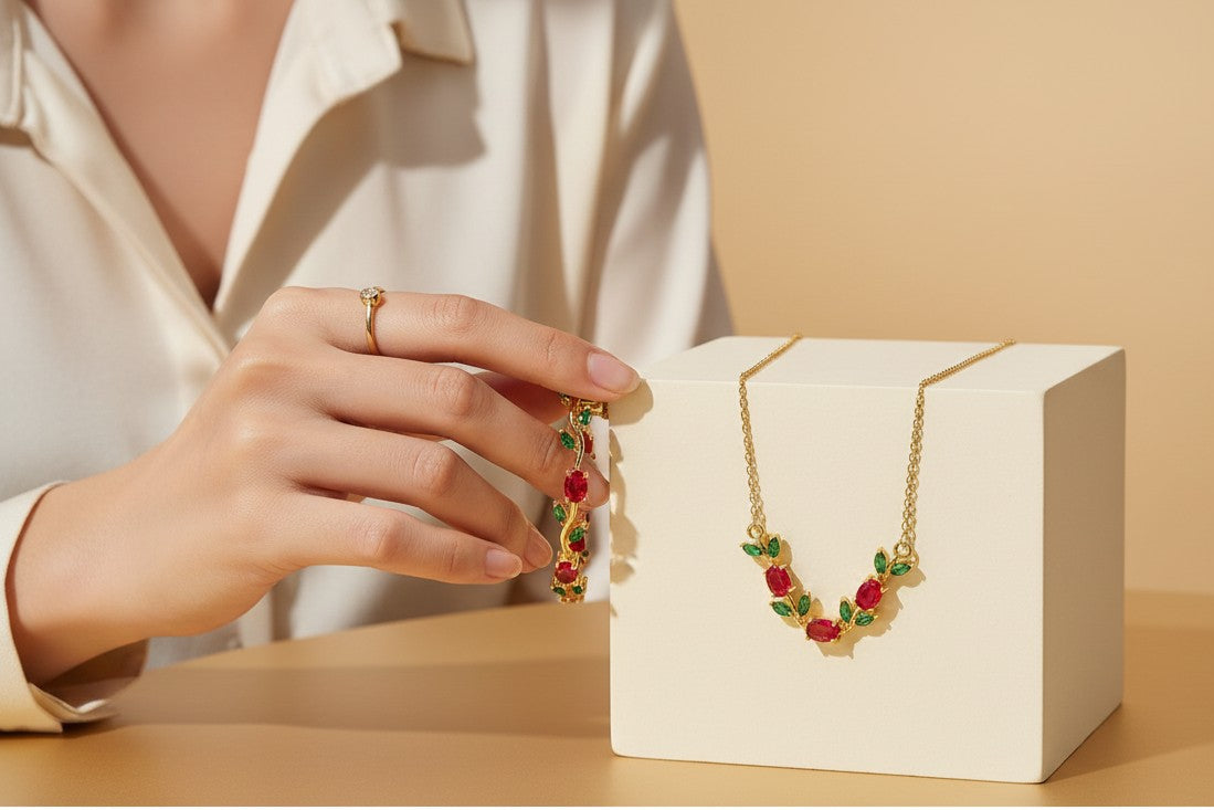 Anti-tarnish, gold-plated Tulip Necklace & Bracelet with Red & Green stones held by a hand.